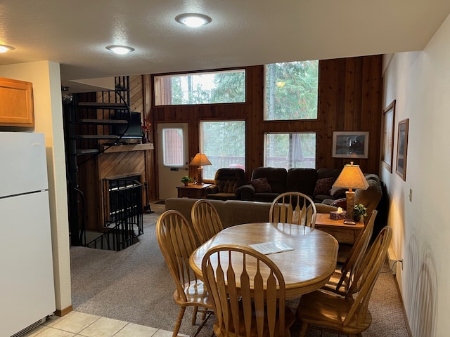 dining area featuring wooden walls, light colored carpet, a fireplace, light tile patterned flooring, and a textured ceiling