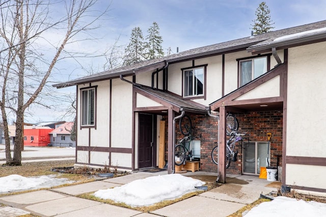 view of front of house featuring stucco siding, brick siding, and roof with shingles