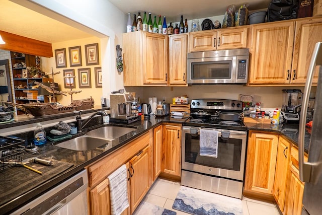 kitchen featuring light tile patterned floors, stainless steel appliances, dark stone counters, and a sink