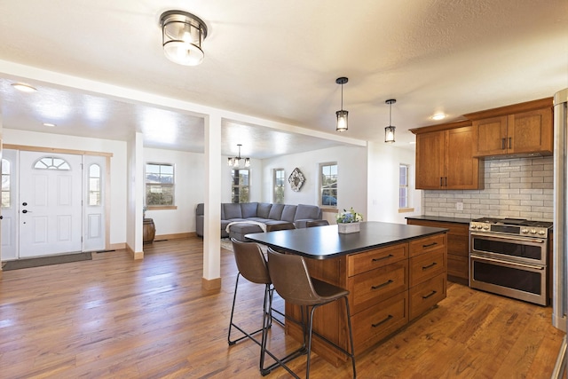 kitchen with tasteful backsplash, dark countertops, wood finished floors, brown cabinetry, and range with two ovens