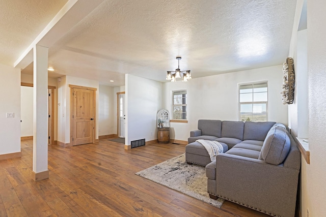 living area featuring visible vents, hardwood / wood-style flooring, a textured ceiling, baseboards, and a chandelier