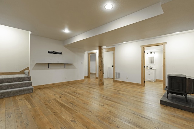 finished basement with visible vents, light wood-style flooring, stairs, and a wood stove