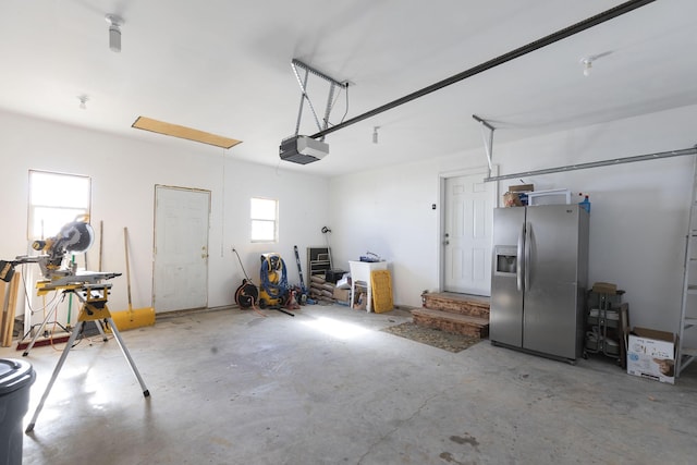 garage with a garage door opener and stainless steel refrigerator with ice dispenser