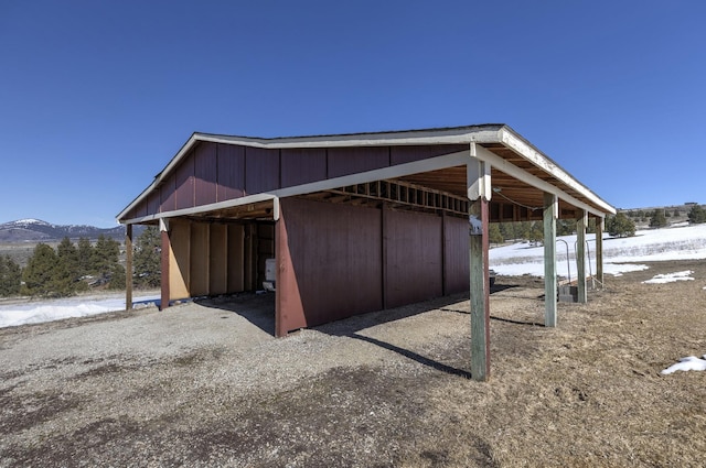 snow covered structure with a mountain view, an outbuilding, and a carport