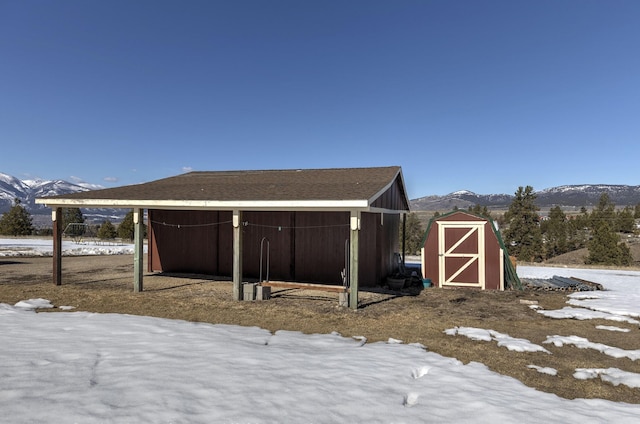 snow covered structure featuring a mountain view, an outbuilding, and a storage shed