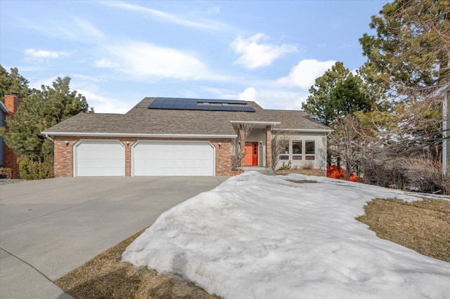 view of front of property featuring brick siding, solar panels, roof with shingles, a garage, and driveway