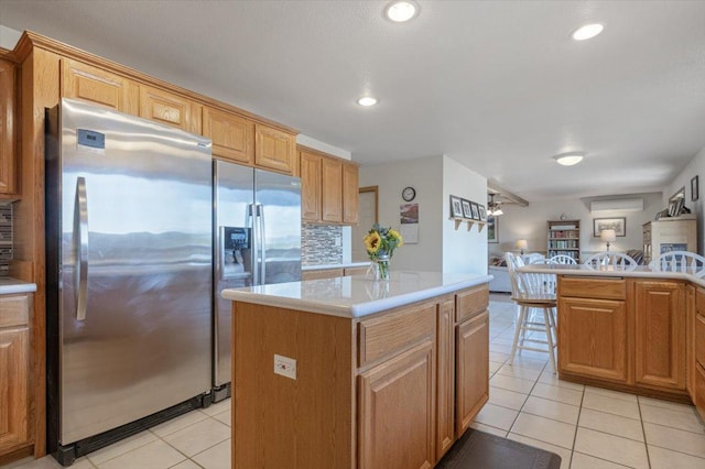 kitchen with a kitchen island, open floor plan, light countertops, light tile patterned floors, and freestanding refrigerator