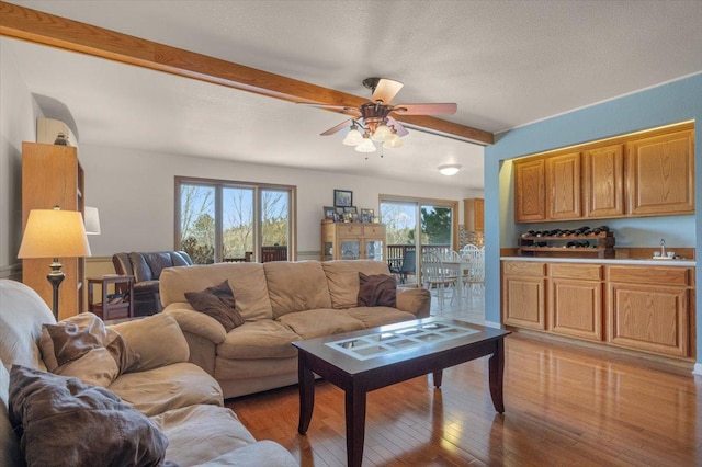 living room with beam ceiling, light wood-style flooring, a textured ceiling, and ceiling fan