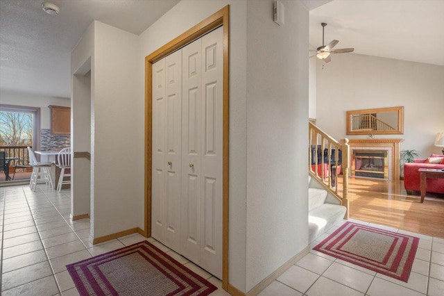 interior space featuring a ceiling fan, a glass covered fireplace, light tile patterned flooring, stairs, and vaulted ceiling