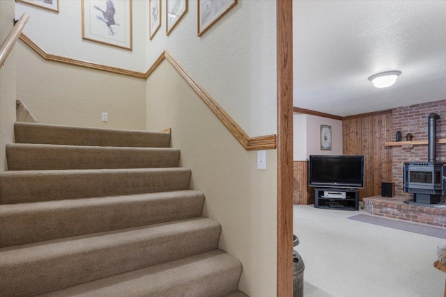 stairs featuring carpet, wood walls, ornamental molding, a wood stove, and a textured ceiling