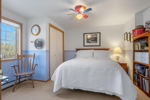 carpeted bedroom featuring a baseboard heating unit, a closet, ceiling fan, and wainscoting