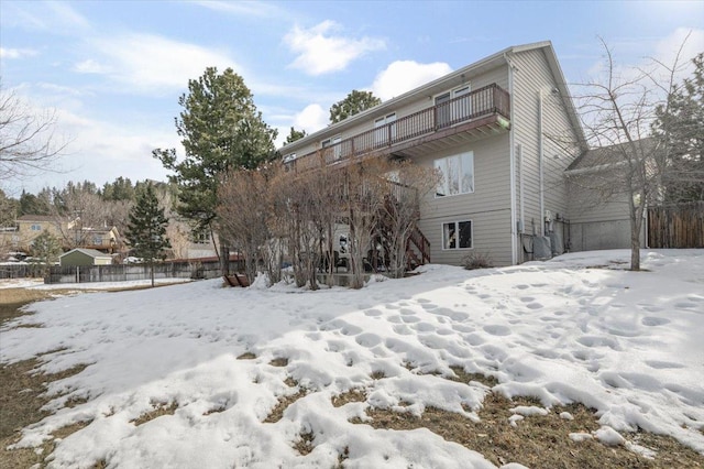 snow covered rear of property with a balcony and fence