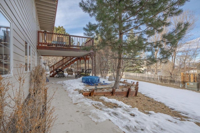 snowy yard featuring a wooden deck, stairs, a patio, and fence