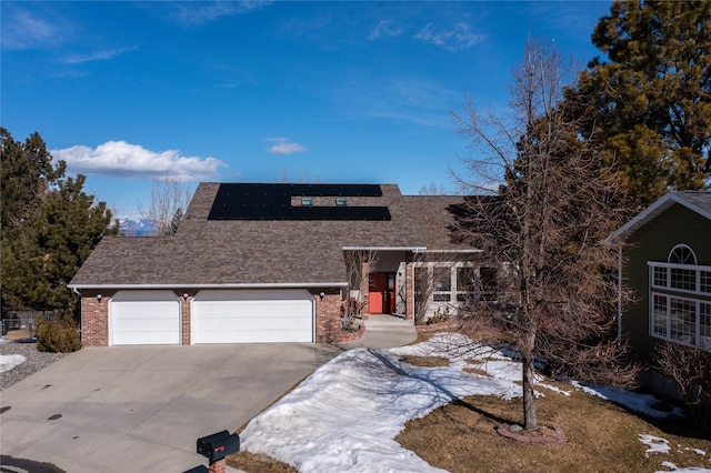 view of front facade with brick siding, roof mounted solar panels, concrete driveway, and a garage