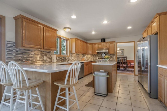 kitchen featuring under cabinet range hood, backsplash, stainless steel appliances, light countertops, and light tile patterned floors