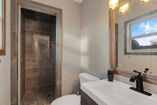 bathroom featuring tiled shower, toilet, vanity, and a textured wall