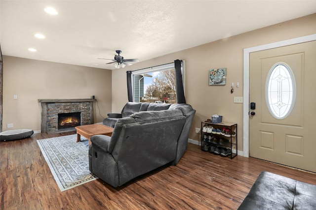 living room with baseboards, a stone fireplace, recessed lighting, dark wood-style floors, and a ceiling fan