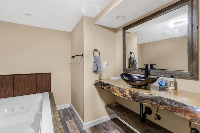 bathroom with a sink, baseboards, wood finished floors, and a whirlpool tub