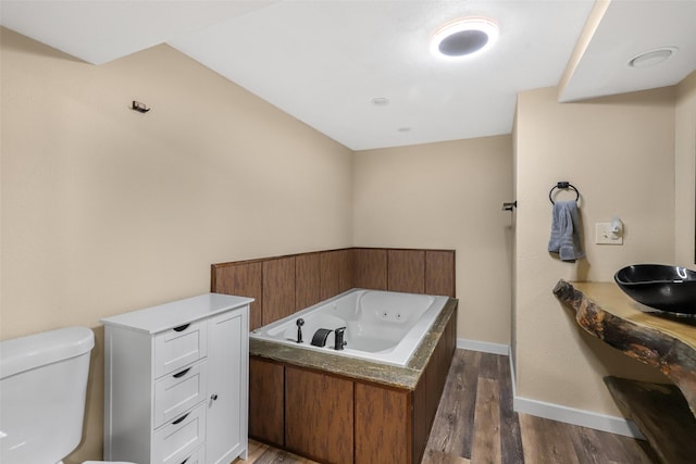 bathroom with toilet, a sink, wood finished floors, baseboards, and a whirlpool tub