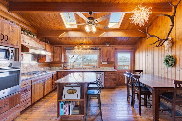 kitchen with brown cabinetry, appliances with stainless steel finishes, a skylight, and under cabinet range hood