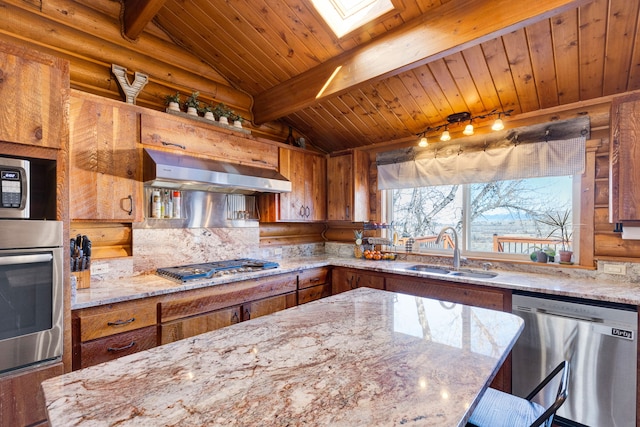 kitchen featuring lofted ceiling with skylight, appliances with stainless steel finishes, exhaust hood, brown cabinetry, and a sink