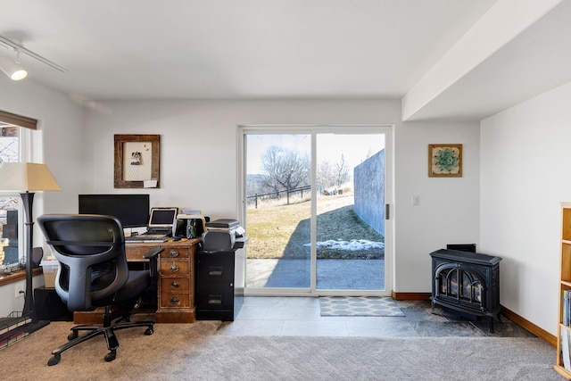 carpeted office space featuring rail lighting, baseboards, a wood stove, and tile patterned floors