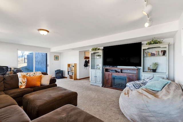 living area with baseboards, a wood stove, rail lighting, a glass covered fireplace, and light colored carpet