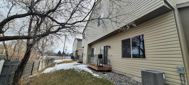 view of snowy exterior with fence and central AC