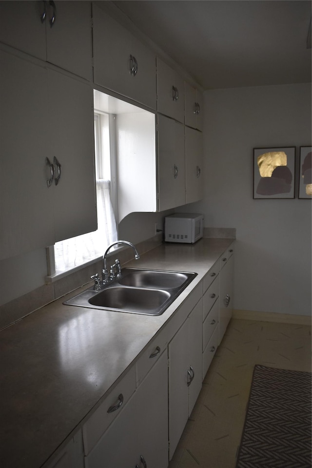 kitchen with a sink, white cabinets, light countertops, baseboards, and white microwave