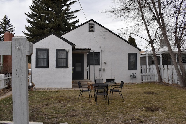 rear view of house featuring stucco siding, a yard, and fence