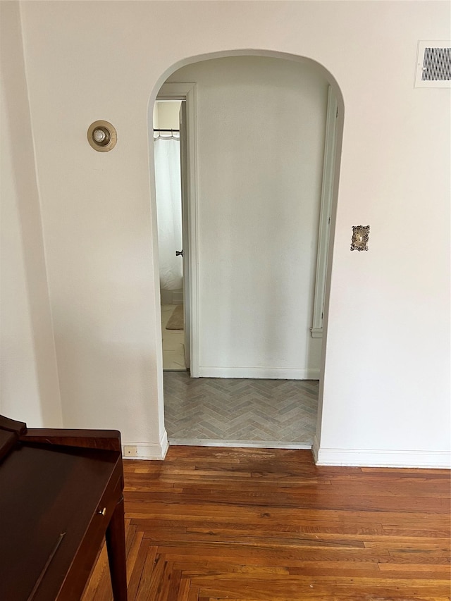 hallway featuring parquet flooring, baseboards, visible vents, and arched walkways