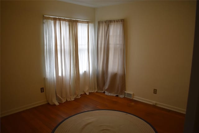 spare room featuring a wealth of natural light, visible vents, baseboards, and wood-type flooring