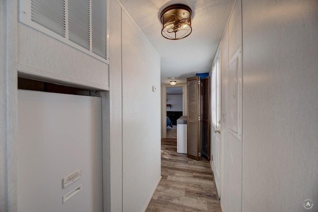 corridor featuring light wood-style flooring, visible vents, and a textured ceiling