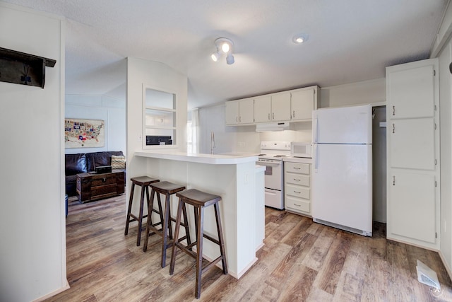 kitchen with white appliances, lofted ceiling, light countertops, light wood-style floors, and a kitchen breakfast bar