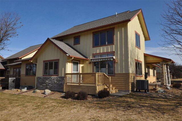 rear view of house with roof with shingles, central AC, stone siding, a lawn, and board and batten siding