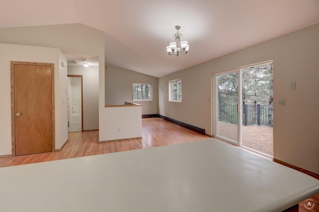 spare room with a notable chandelier, light wood finished floors, a baseboard radiator, baseboards, and vaulted ceiling