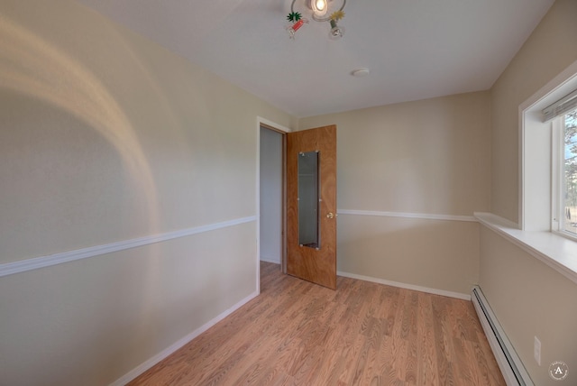 spare room featuring a baseboard heating unit, wood finished floors, and baseboards