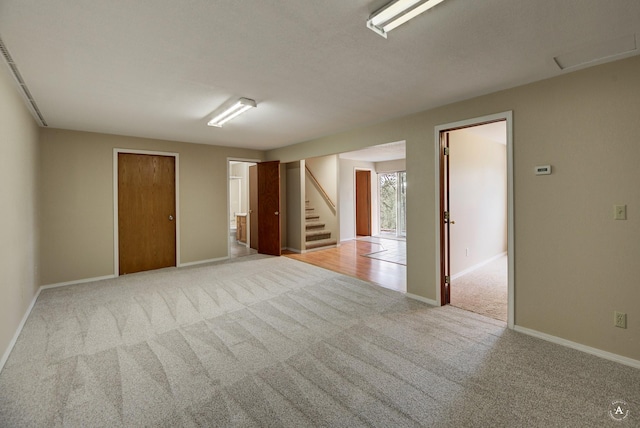 unfurnished room featuring stairway, light colored carpet, and baseboards