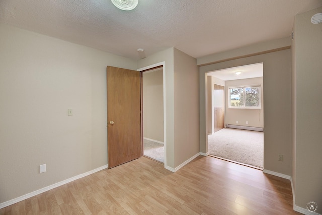 spare room with a textured ceiling, light wood-style flooring, baseboards, and a baseboard radiator