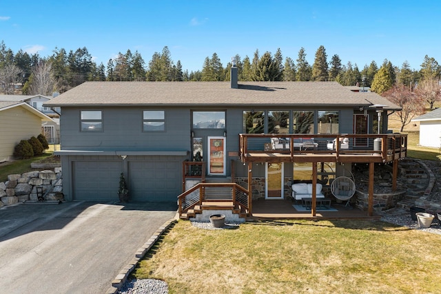 view of front facade featuring a shingled roof, aphalt driveway, a front yard, a deck, and an attached garage