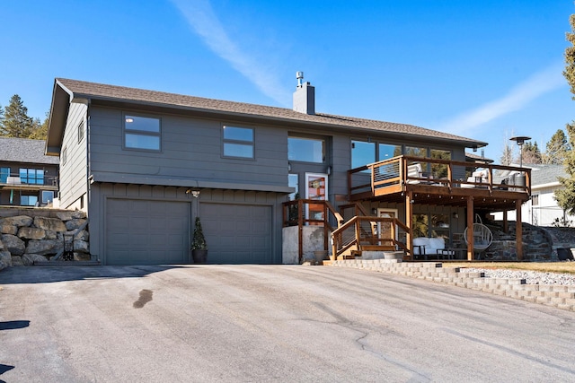 view of front of house featuring an attached garage, a chimney, a deck, aphalt driveway, and board and batten siding