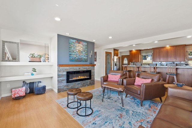 living room with a glass covered fireplace, recessed lighting, light wood-type flooring, and baseboards