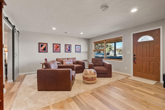 living room with a barn door, recessed lighting, light wood-style floors, and baseboards