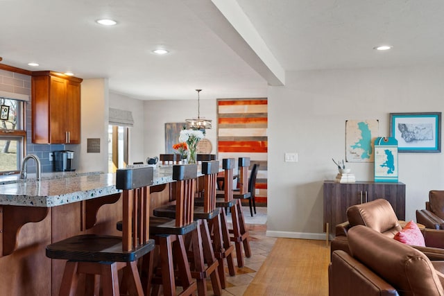 kitchen featuring light stone counters, brown cabinetry, recessed lighting, a kitchen breakfast bar, and open floor plan