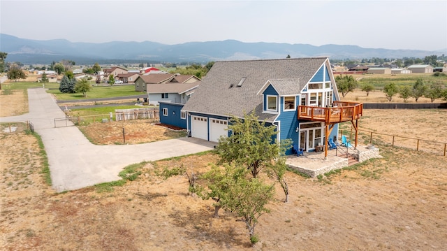 view of front facade featuring a deck with mountain view, concrete driveway, fence, and a shingled roof