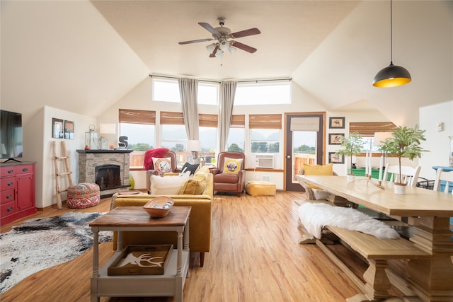 living room featuring light wood-type flooring, high vaulted ceiling, a stone fireplace, and ceiling fan