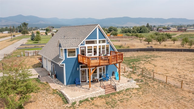 rear view of house with a rural view, a deck with mountain view, fence, and a shingled roof