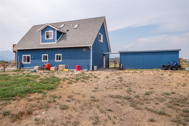 back of property with a pole building, an outdoor structure, roof with shingles, and fence