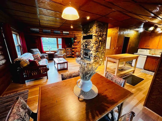 dining area with a stone fireplace, light wood-style flooring, and wooden ceiling