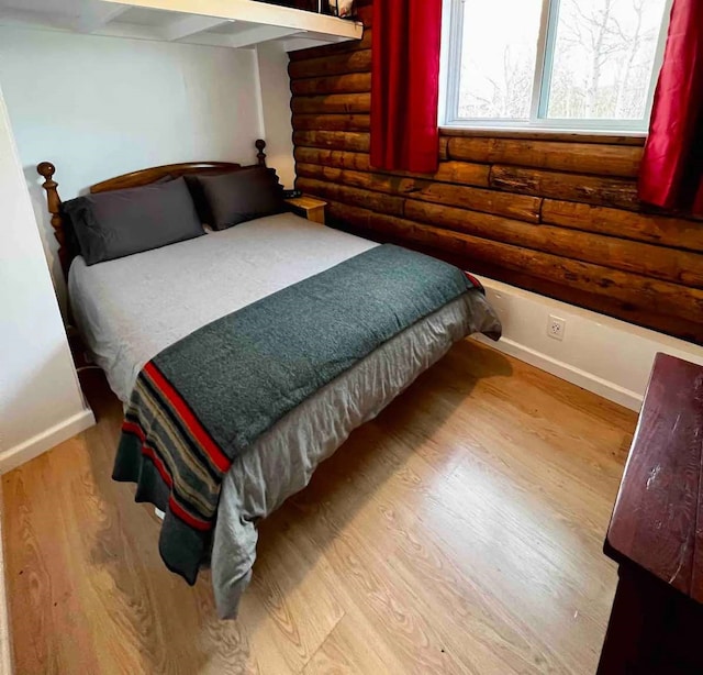 bedroom featuring log walls, baseboards, and wood finished floors